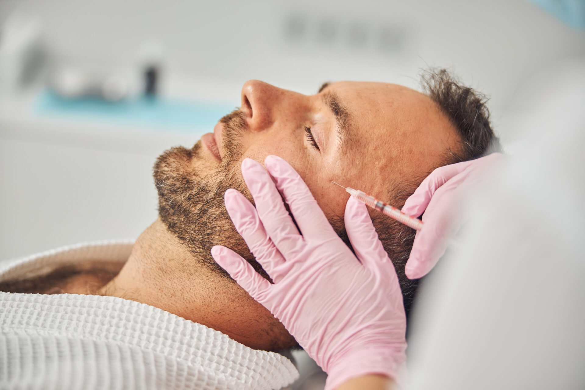 Close up of female cosmetologist hands in sterile gloves making injection into man face