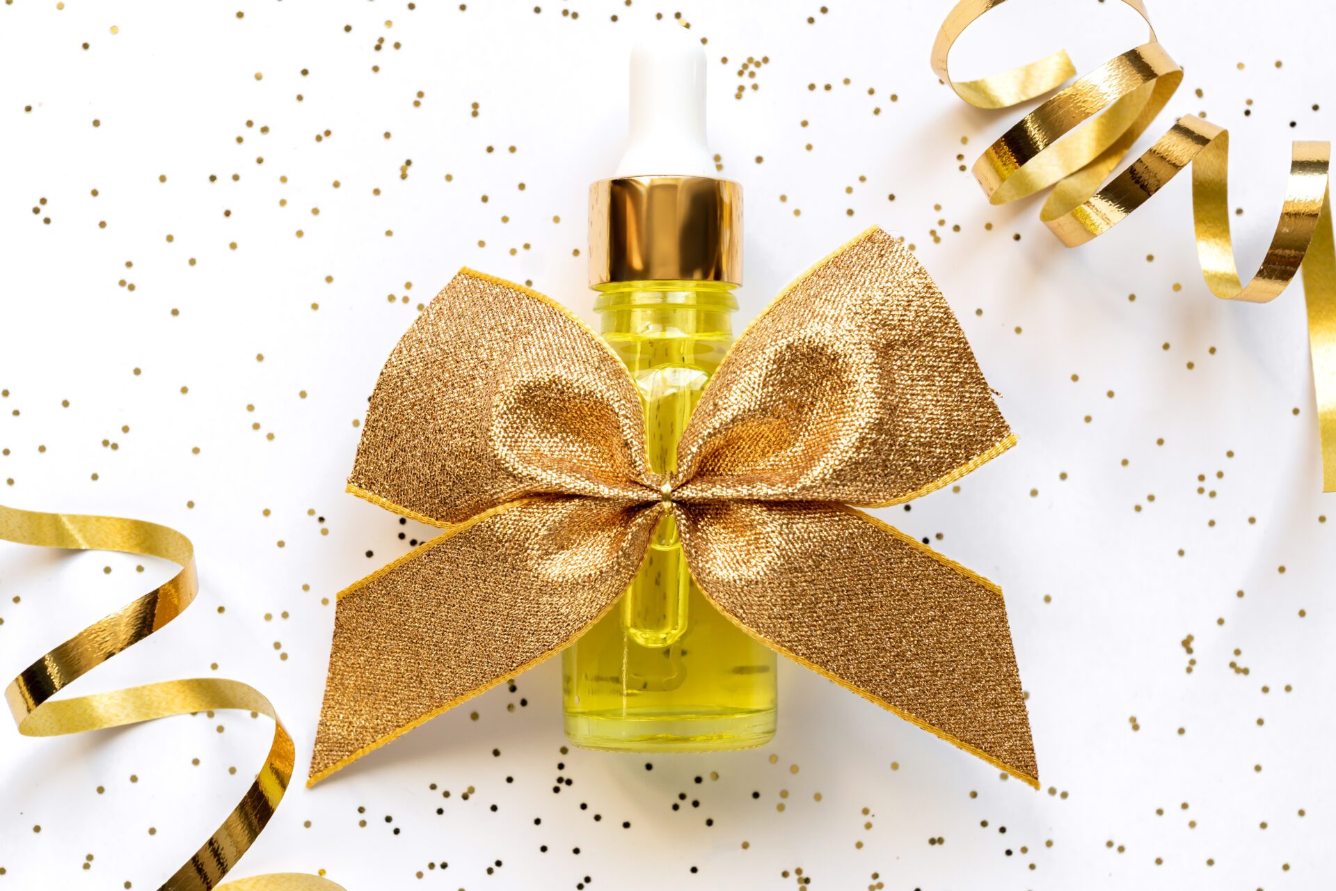 Top view of beauty face oil with golden tied bow as holiday present. Festive presentation for skin care ptoducts. Beauty cosmetic product for skincare concept.