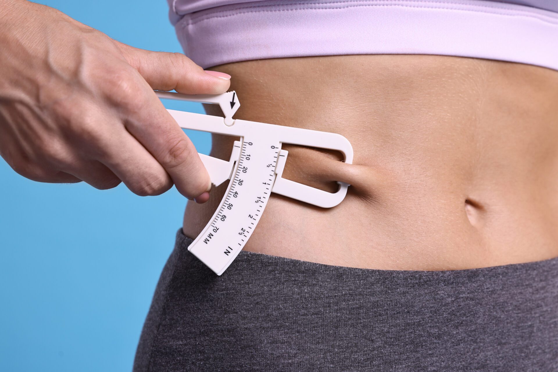 Woman measuring body fat with caliper on light blue background, closeup