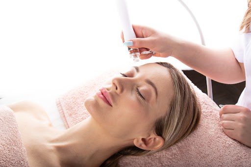 Aesthetician performing a skincare treatment on a client lying down